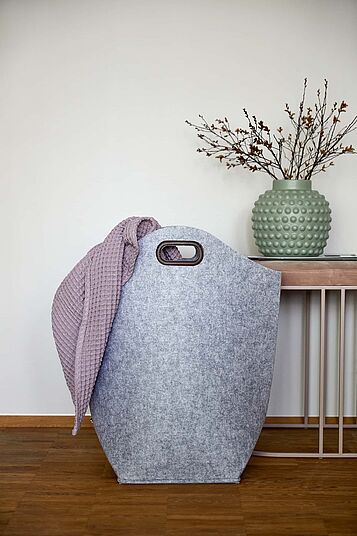 Ein Wäschesammler aus Filz in der Farbe grau vor einem wohnlichem Hintergrund